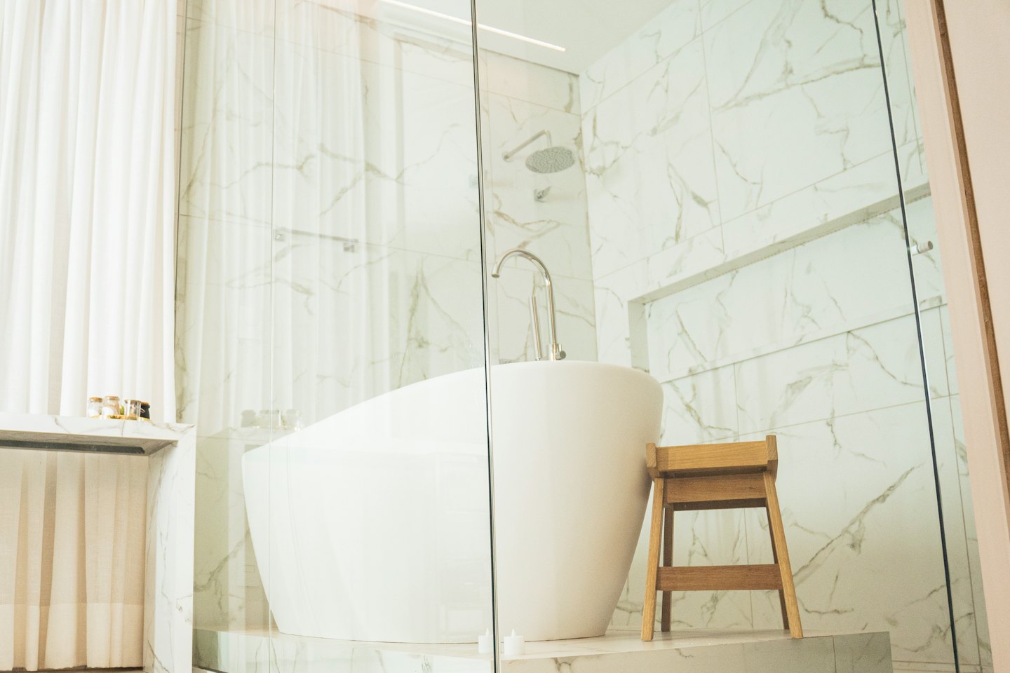 Freestanding bathtub and wooden stool in a modern bathroom.