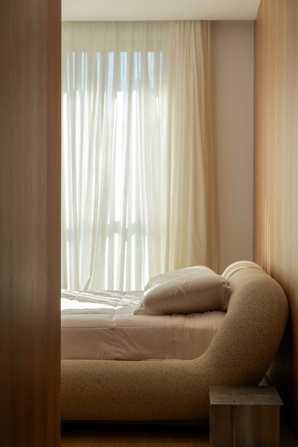 Bedroom with a curved upholstered bed and sheer curtains.
