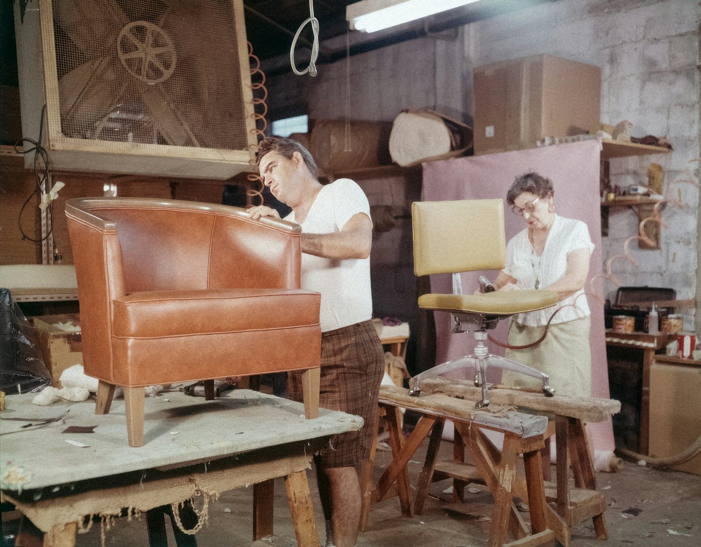 Two craftspeople work on upholstered chairs inside a rustic workshop.